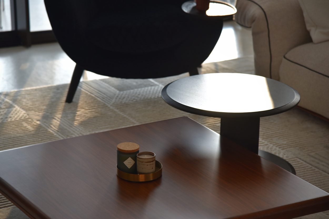 A walnut low table with candles on a brass tray, hard afternoon light across a black side table