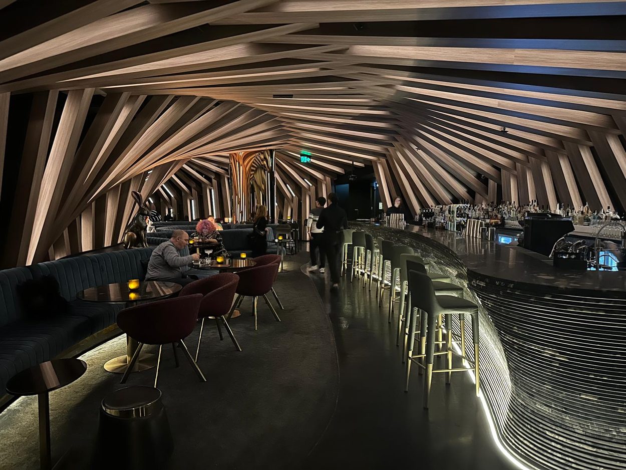 The finished hotel bar at night, ribbed timber ceiling lit, guests at the counter
