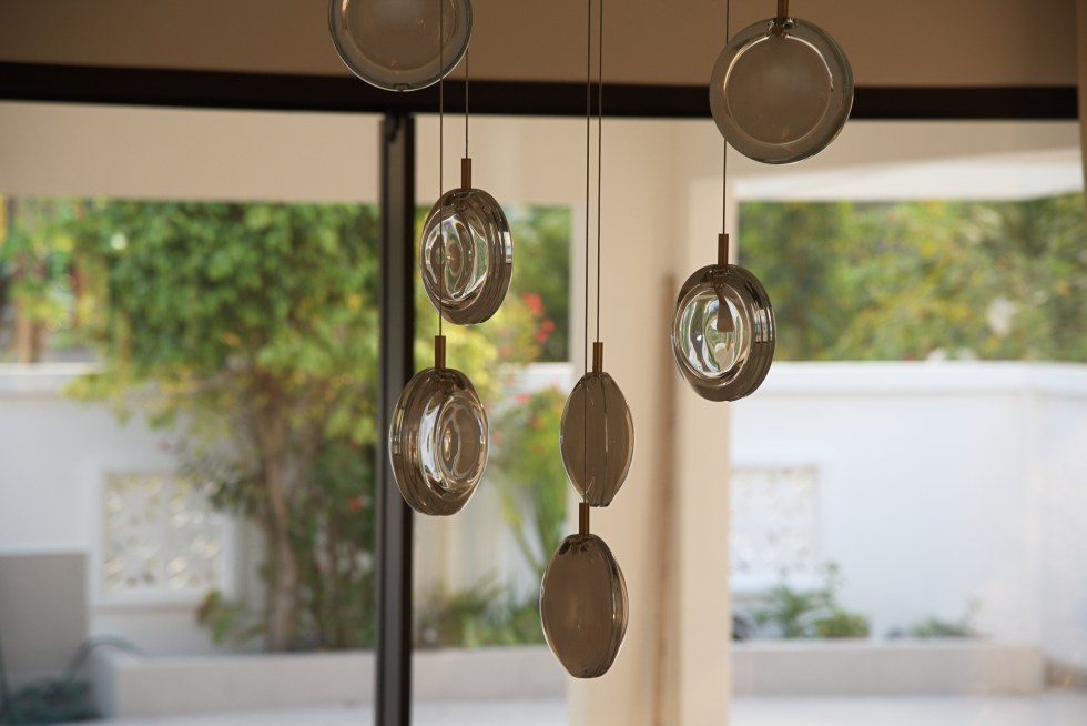 Glass pendants hanging against black-framed glazing and dense garden planting